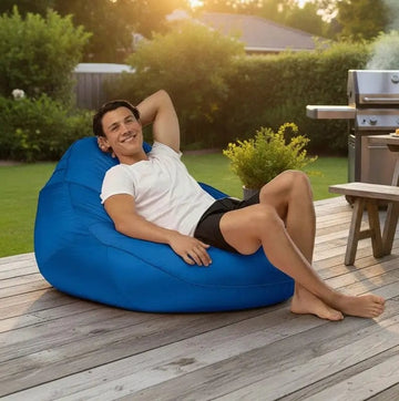 Man relaxing on a blue bean bag chair outdoors on a wooden deck.