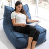 Woman reading a book on a large blue bean bag chair in a bright room.