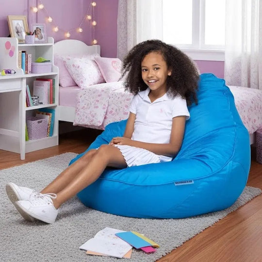 Young girl sitting on a blue bean bag chair in a bedroom with pink walls and white furniture.