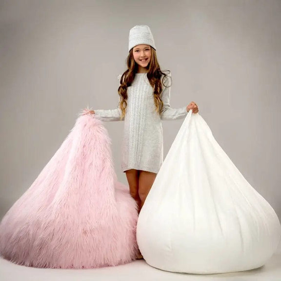 Child holding a pink and a white bean bag chair against a plain background
