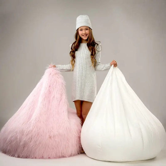 Child holding a pink and a white bean bag chair against a plain background