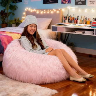Girl sitting on a pink fluffy bean bag chair in a bedroom with a desk and decor.