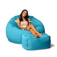 Woman sitting on a large blue bean bag chair with a smaller matching ottoman on a white background