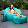 Woman sitting on a large turquoise bean bag chair outdoors with plants in the background