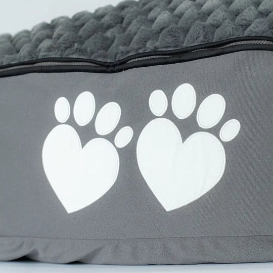 Gray pet bed with white paw prints shaped like hearts on a light gray background